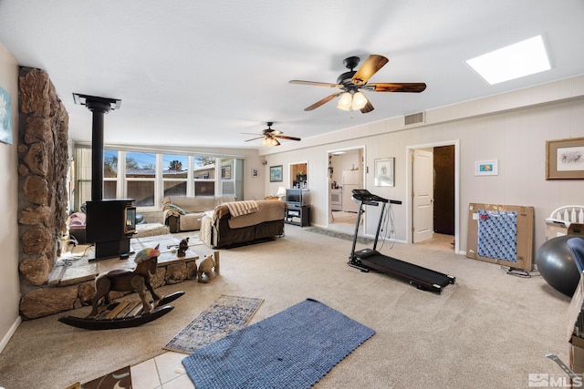 exercise area with ceiling fan, light carpet, and a wood stove