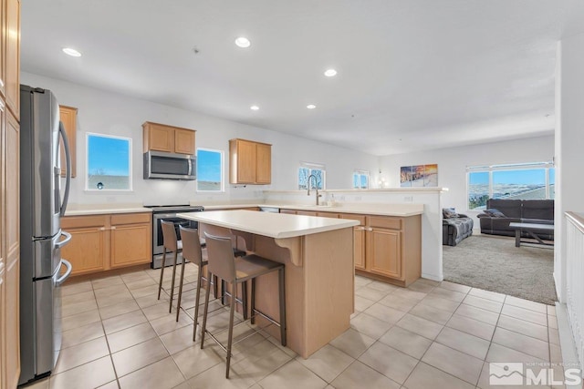 kitchen with appliances with stainless steel finishes, a breakfast bar, sink, a center island, and light colored carpet