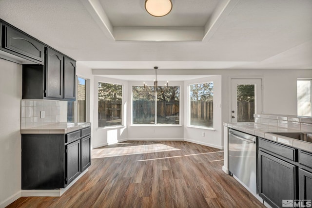 kitchen with pendant lighting, dark wood-type flooring, dishwasher, a tray ceiling, and decorative backsplash