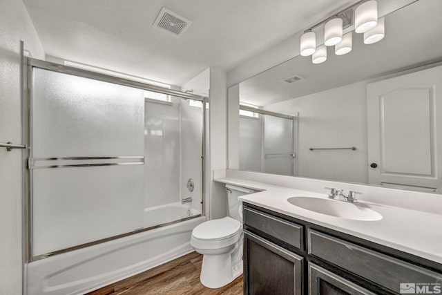 full bathroom featuring vanity, hardwood / wood-style flooring, shower / bath combination with glass door, and toilet