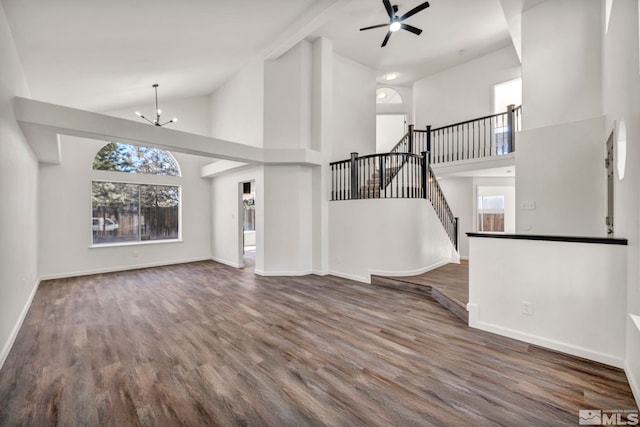 unfurnished living room with ceiling fan with notable chandelier, dark hardwood / wood-style flooring, and high vaulted ceiling