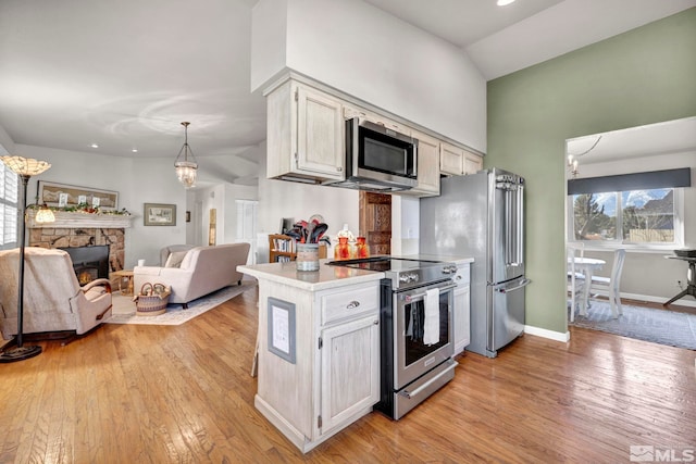 kitchen with appliances with stainless steel finishes, white cabinetry, a fireplace, light hardwood / wood-style floors, and decorative light fixtures