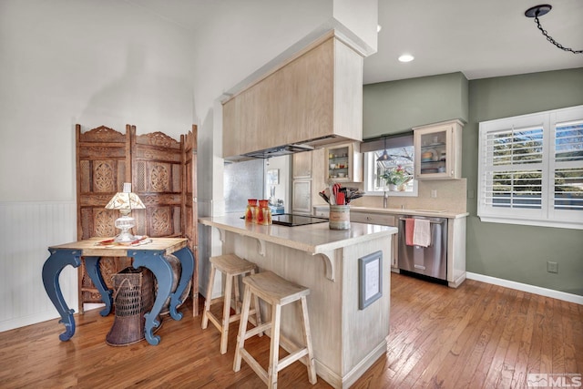 kitchen featuring light hardwood / wood-style flooring, a kitchen breakfast bar, black electric stovetop, stainless steel dishwasher, and kitchen peninsula