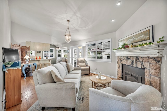 living room with vaulted ceiling, a stone fireplace, and light wood-type flooring