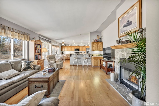 living room featuring lofted ceiling, a fireplace, and light wood-type flooring