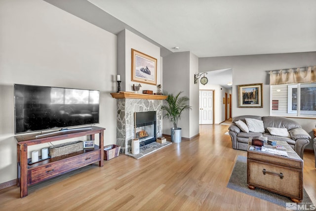 living room featuring hardwood / wood-style floors, a stone fireplace, and vaulted ceiling