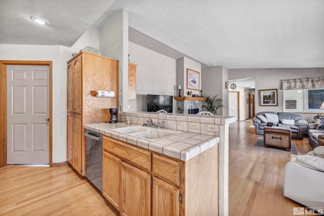 kitchen with lofted ceiling, sink, stainless steel dishwasher, tile counters, and kitchen peninsula