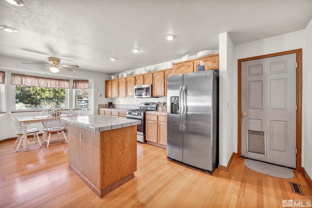 kitchen featuring appliances with stainless steel finishes, tile counters, a center island, and light wood-type flooring