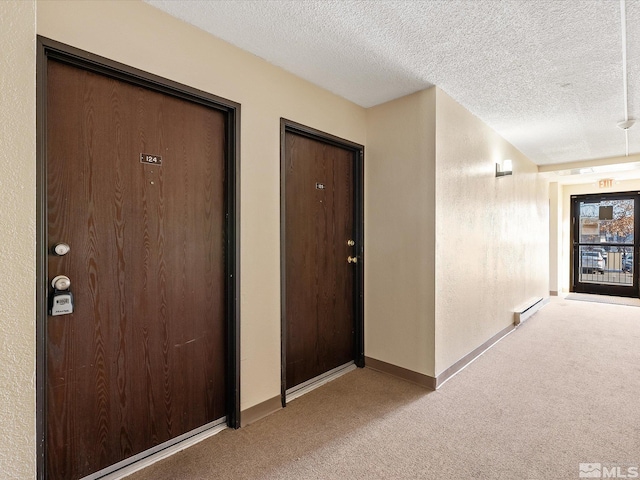 hall with a baseboard heating unit, light colored carpet, and a textured ceiling