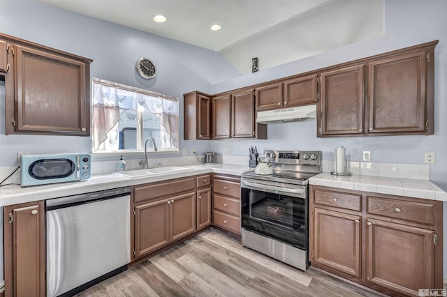 kitchen with appliances with stainless steel finishes, sink, tile countertops, and light wood-type flooring