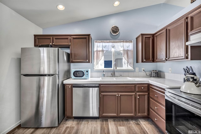 kitchen with lofted ceiling, sink, stainless steel appliances, dark brown cabinetry, and light wood-type flooring