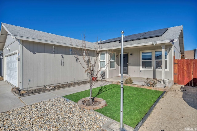 single story home featuring a garage, a front lawn, solar panels, and covered porch