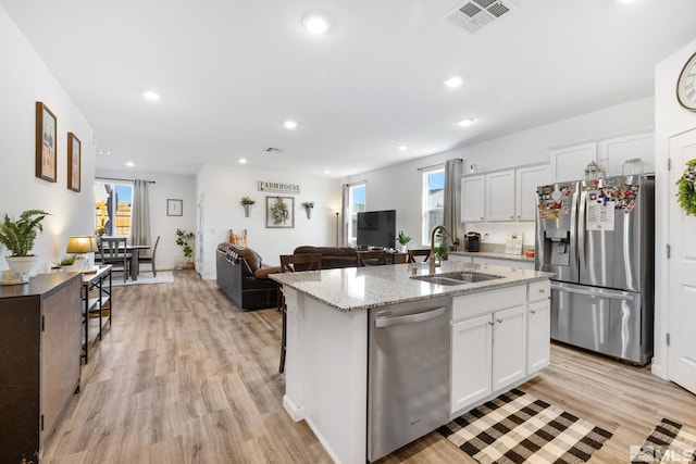 kitchen with appliances with stainless steel finishes, a kitchen island with sink, sink, and white cabinets