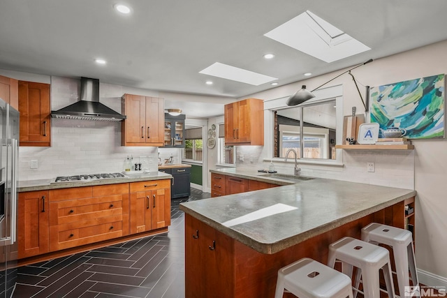 kitchen featuring wall chimney range hood, sink, a breakfast bar, kitchen peninsula, and stainless steel gas stovetop