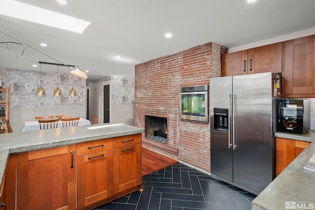 kitchen with a skylight, decorative light fixtures, light stone counters, stainless steel appliances, and a brick fireplace