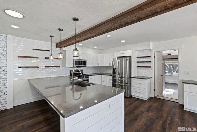 kitchen with appliances with stainless steel finishes, beamed ceiling, white cabinetry, dark stone counters, and kitchen peninsula