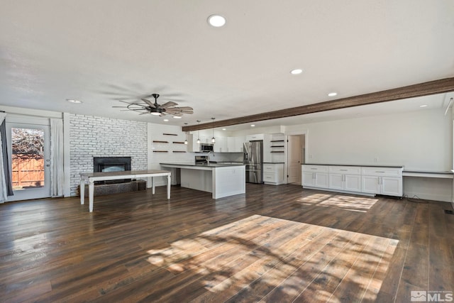 unfurnished living room featuring dark hardwood / wood-style flooring, beam ceiling, a fireplace, and ceiling fan