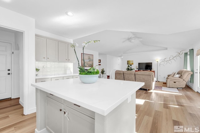 kitchen with lofted ceiling, ceiling fan, tasteful backsplash, a kitchen island, and light wood-type flooring