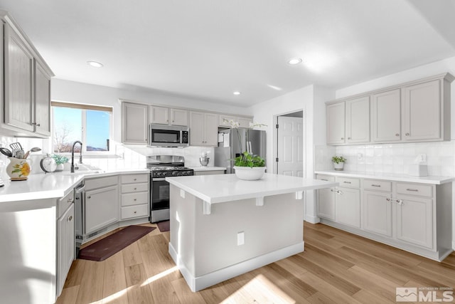 kitchen featuring sink, appliances with stainless steel finishes, a center island, light hardwood / wood-style floors, and decorative backsplash