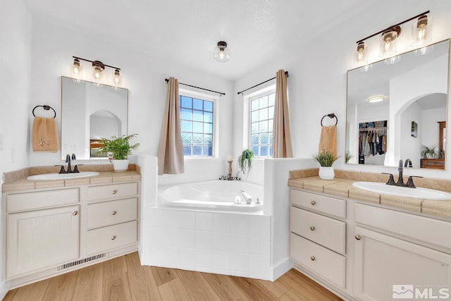 bathroom with hardwood / wood-style flooring, vanity, and a relaxing tiled tub