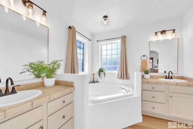 bathroom with hardwood / wood-style flooring, vanity, and tiled bath