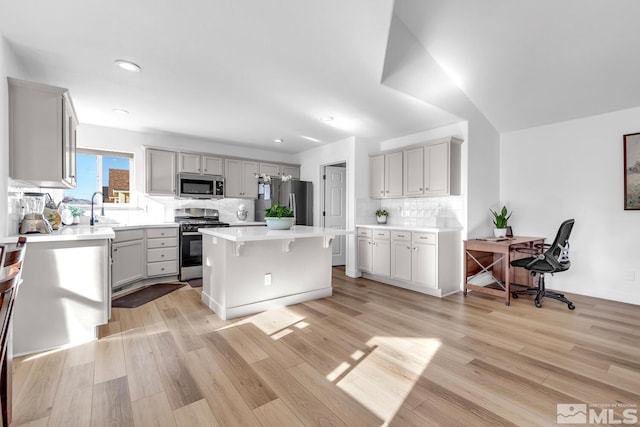 kitchen featuring backsplash, a kitchen breakfast bar, stainless steel appliances, a center island, and light hardwood / wood-style floors