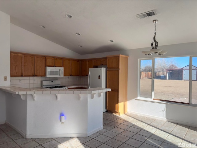 kitchen featuring a breakfast bar area, tile counters, white appliances, and decorative light fixtures