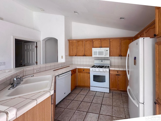 kitchen with sink, white appliances, tasteful backsplash, tile counters, and vaulted ceiling