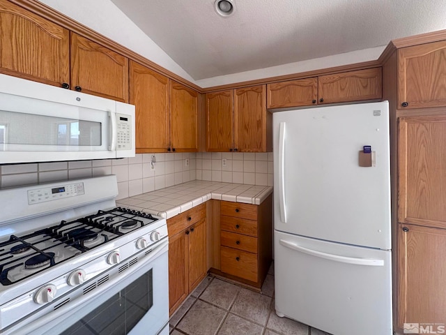 kitchen with vaulted ceiling, tile countertops, decorative backsplash, white appliances, and a textured ceiling