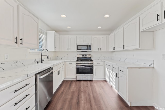 kitchen featuring sink, appliances with stainless steel finishes, white cabinetry, dark hardwood / wood-style floors, and light stone countertops