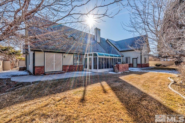 back of property with a sunroom, a yard, and a patio area