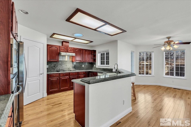 kitchen with sink, black stovetop, light hardwood / wood-style floors, and kitchen peninsula