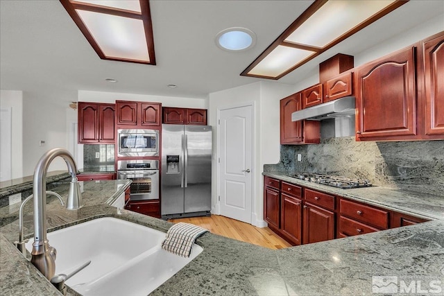 kitchen featuring sink, light wood-type flooring, appliances with stainless steel finishes, stone counters, and backsplash