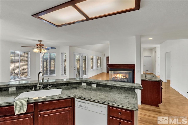 kitchen featuring white dishwasher, sink, light wood-type flooring, and a multi sided fireplace