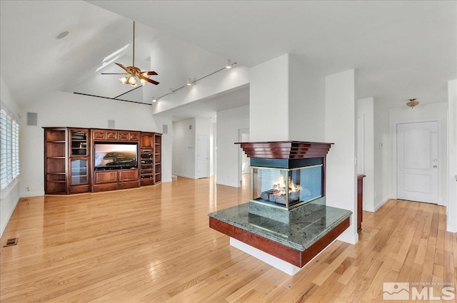 living room with ceiling fan, a multi sided fireplace, track lighting, and light hardwood / wood-style flooring