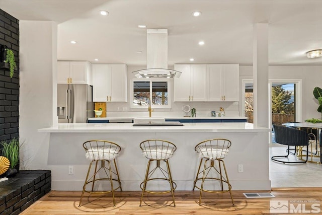 kitchen with white cabinets, a kitchen breakfast bar, island exhaust hood, kitchen peninsula, and stainless steel refrigerator with ice dispenser