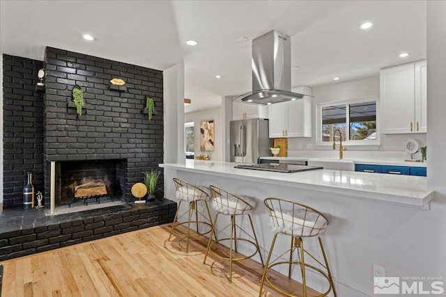 kitchen featuring island range hood, sink, high end refrigerator, white cabinets, and black electric cooktop