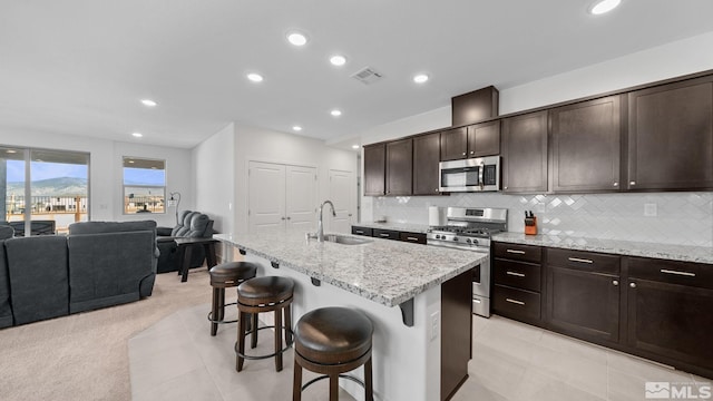 kitchen with appliances with stainless steel finishes, an island with sink, sink, a kitchen bar, and light stone countertops