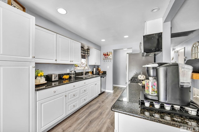 kitchen featuring sink, dark stone countertops, light wood-type flooring, appliances with stainless steel finishes, and white cabinets