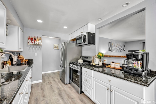 kitchen featuring appliances with stainless steel finishes, white cabinetry, sink, dark stone countertops, and light hardwood / wood-style flooring