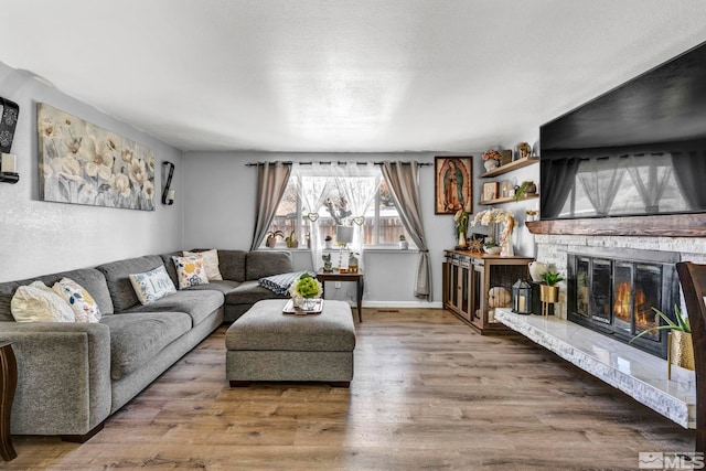 living room with a stone fireplace, wood-type flooring, and a textured ceiling