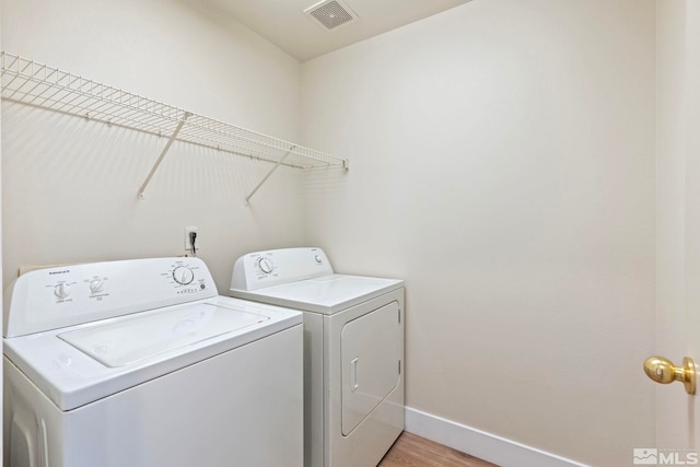 clothes washing area featuring washing machine and clothes dryer and light wood-type flooring