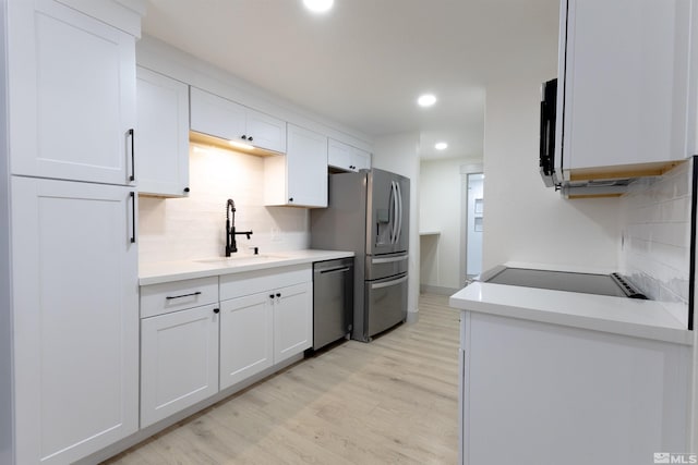 kitchen featuring sink, white cabinets, decorative backsplash, light hardwood / wood-style floors, and stainless steel appliances