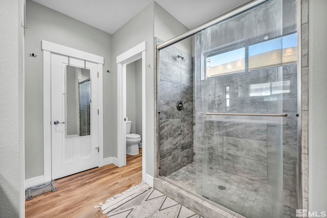 bathroom featuring a shower stall, toilet, baseboards, and wood finished floors