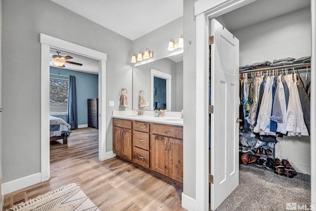 bathroom with a walk in closet, double vanity, ensuite bathroom, wood finished floors, and a sink