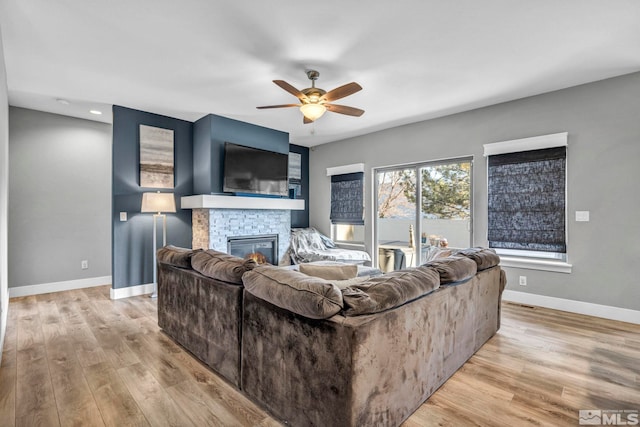 living room with a fireplace, baseboards, light wood-style floors, and a ceiling fan