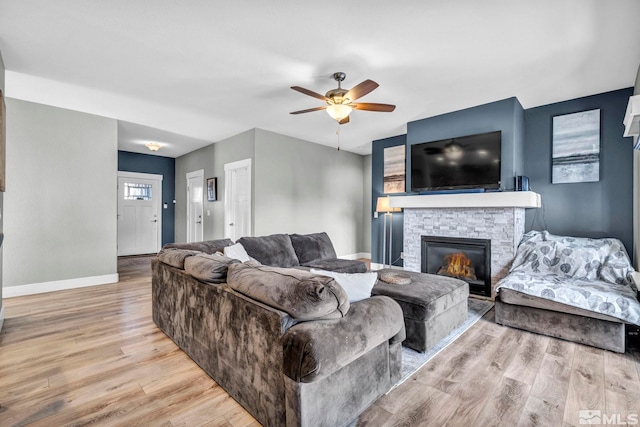 living room featuring ceiling fan, a fireplace, baseboards, and wood finished floors