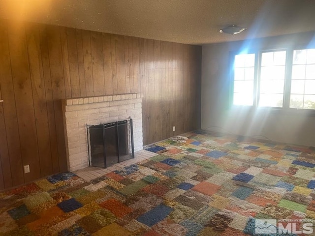 unfurnished living room featuring a brick fireplace, carpet, a textured ceiling, and wood walls