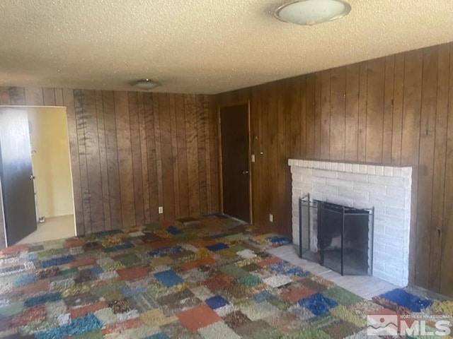 unfurnished living room with wooden walls, a brick fireplace, and a textured ceiling