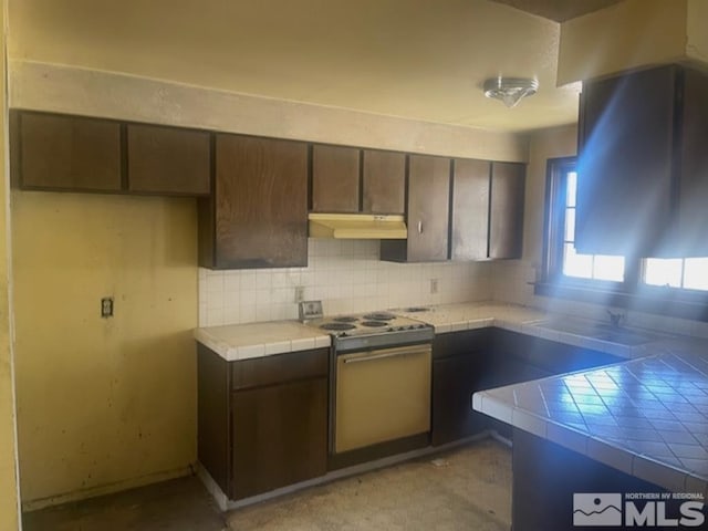 kitchen with tasteful backsplash, white electric range, tile countertops, and dark brown cabinetry